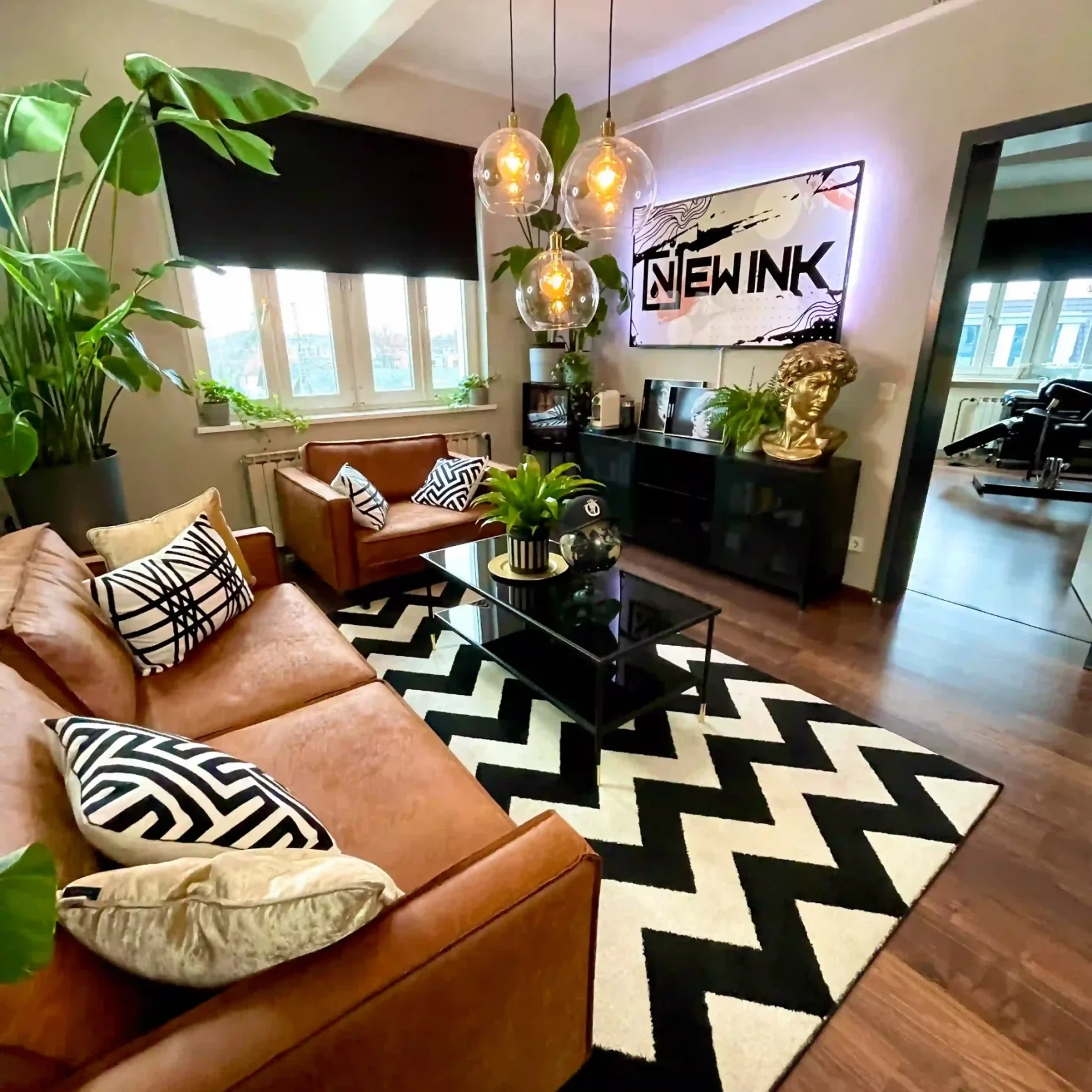 Ein stilvoll eingerichteter Lounge-Bereich im Nextink Tattoo Studio Berlin, mit Leder-Sofas, Pflanzen und modernen Beleuchtungselementen.